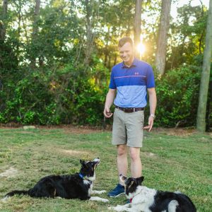 a man standing in a grassy area with two dogs
